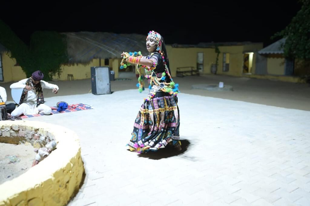 Una persona bailando con un atuendo tradicional y colorido al aire libre, con edificios en el fondo.