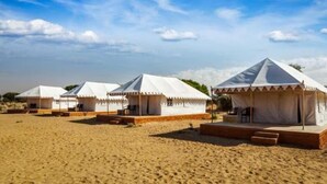 Une rangée de tentes blanches à toit plat, installées sur une plage de sable fin, sous un ciel dégagé.
