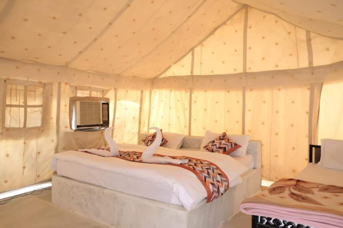 A tented room with a bed, air conditioning unit, and curtains.