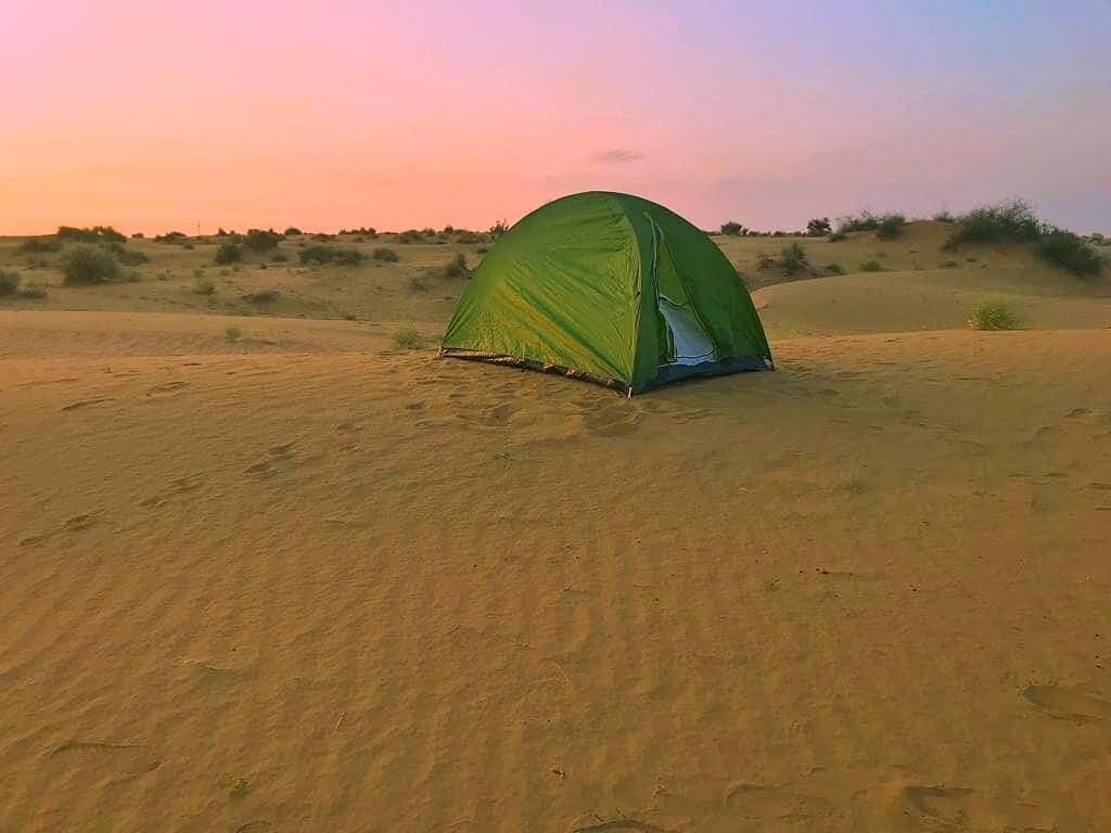 A green tent in a desert landscape at sunset.