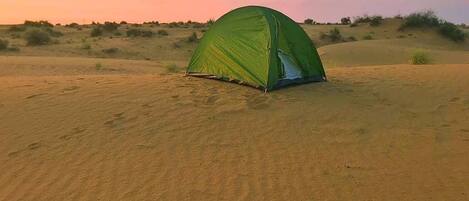 A green tent in a desert landscape at sunset.