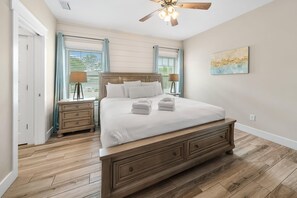 A bedroom with a wooden bed, two bedside tables, a ceiling fan, and a window with curtains. - Laid Back In Laguna - Pet Friendly, Private Pool (Panama City Beach)