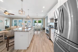A modern kitchen with a large stainless steel refrigerator, a central island with a sink, and pendant lighting. - Laid Back In Laguna - Pet Friendly, Private Pool (Panama City Beach)