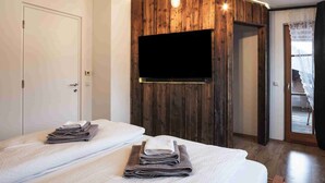 A modern hotel room with a wooden accent wall, a mounted TV, and two beds with towels. - Luxury Larch Loft, perfect for groups/family of up to 6 people

 (Tesido BZ)