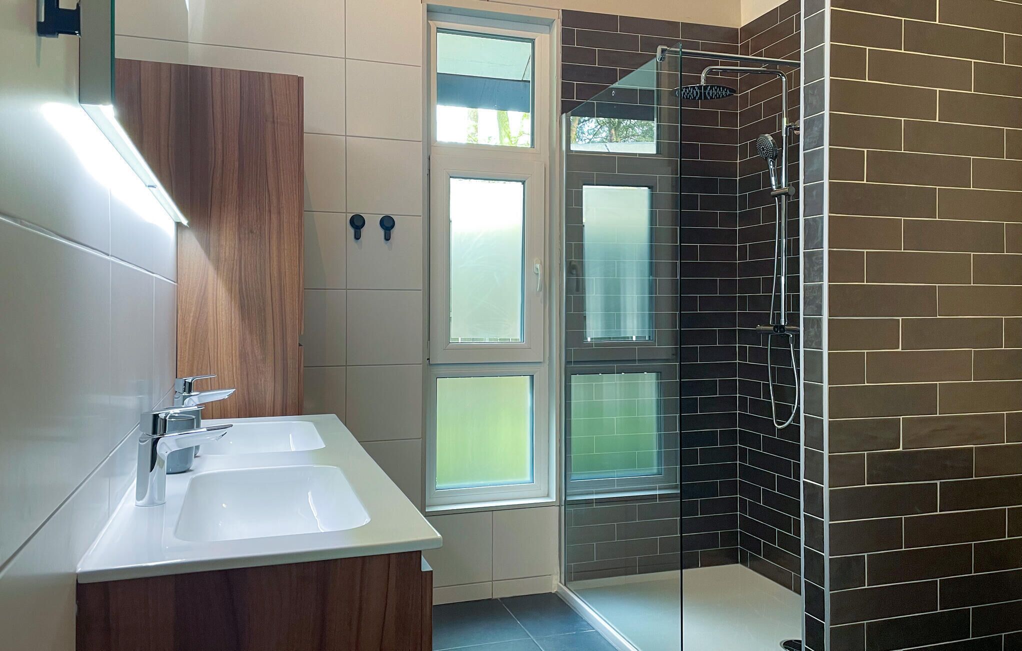 Ein Badezimmer mit zwei Waschbecken, einem Spiegel und einer Duschkabine mit Glastür.