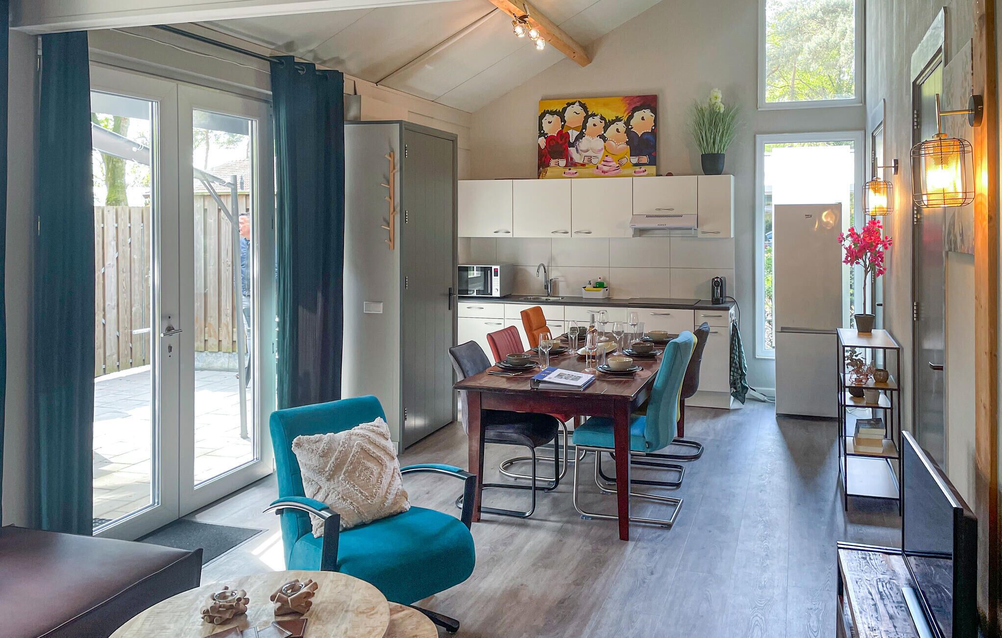 A modern kitchen with white cabinets, a dining area with a wooden table and blue chairs, and a large window with curtains.