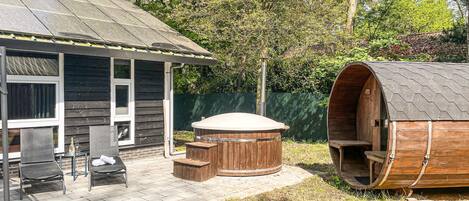 Een houten jacuzzi en een sauna in een achtertuin met een huis.