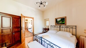Een slaapkamer met een bed, een bankje, een bureau, een stoel, een kledingkast en een schilderij aan de muur.