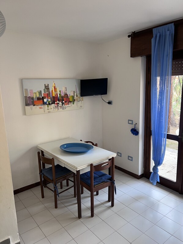 Ein Essbereich mit einem weißen Tisch, blauen Stühlen und einem blauen Teller. Ein Flachbildfernseher ist über dem Tisch an der Wand befestigt.