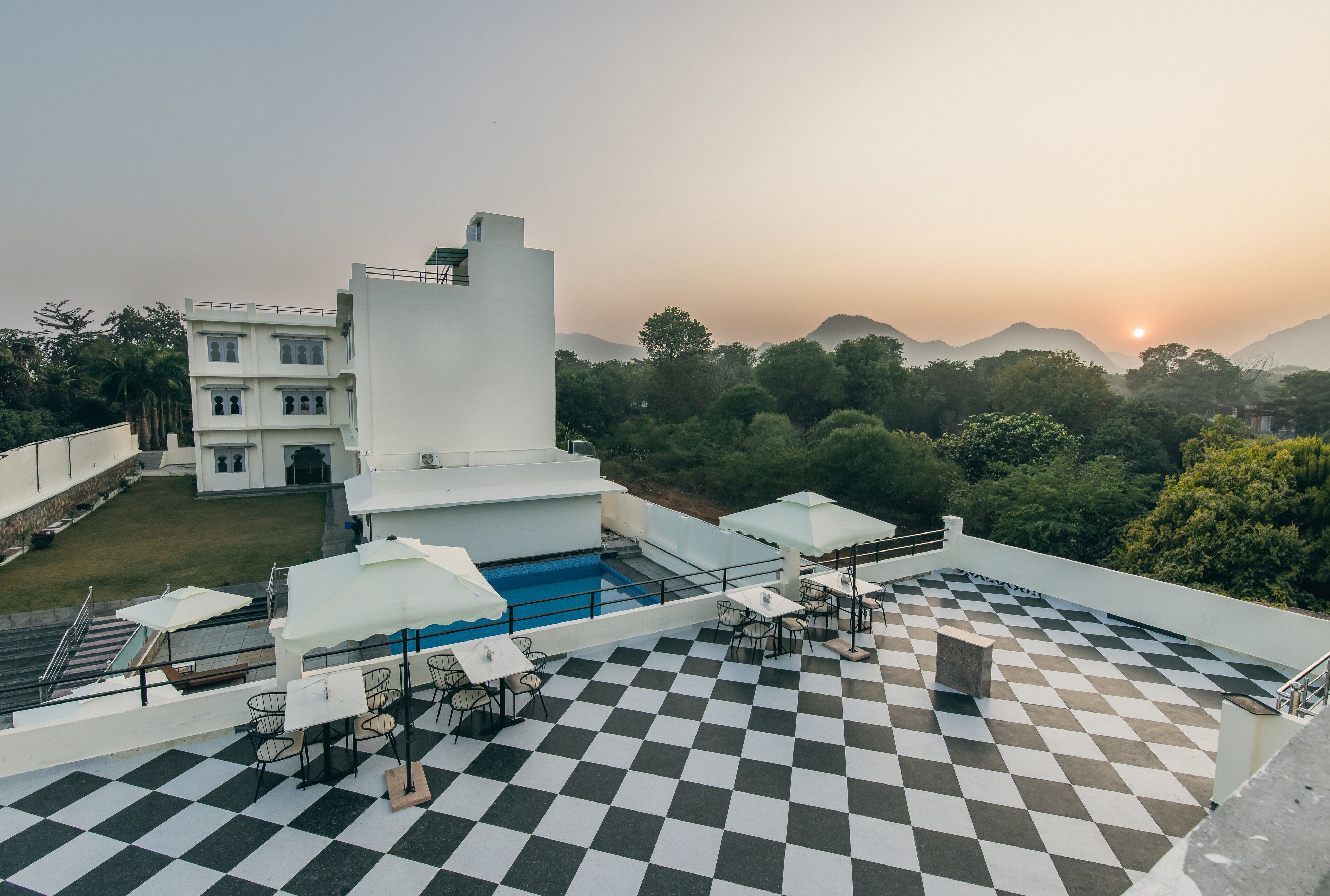 A rooftop terrace with a checkered floor, outdoor seating, a pool, and a view of the surrounding landscape.