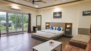 Habitación de hotel con cama, sofá, mesa, ventilador de techo y balcón con vistas a zonas verdes.