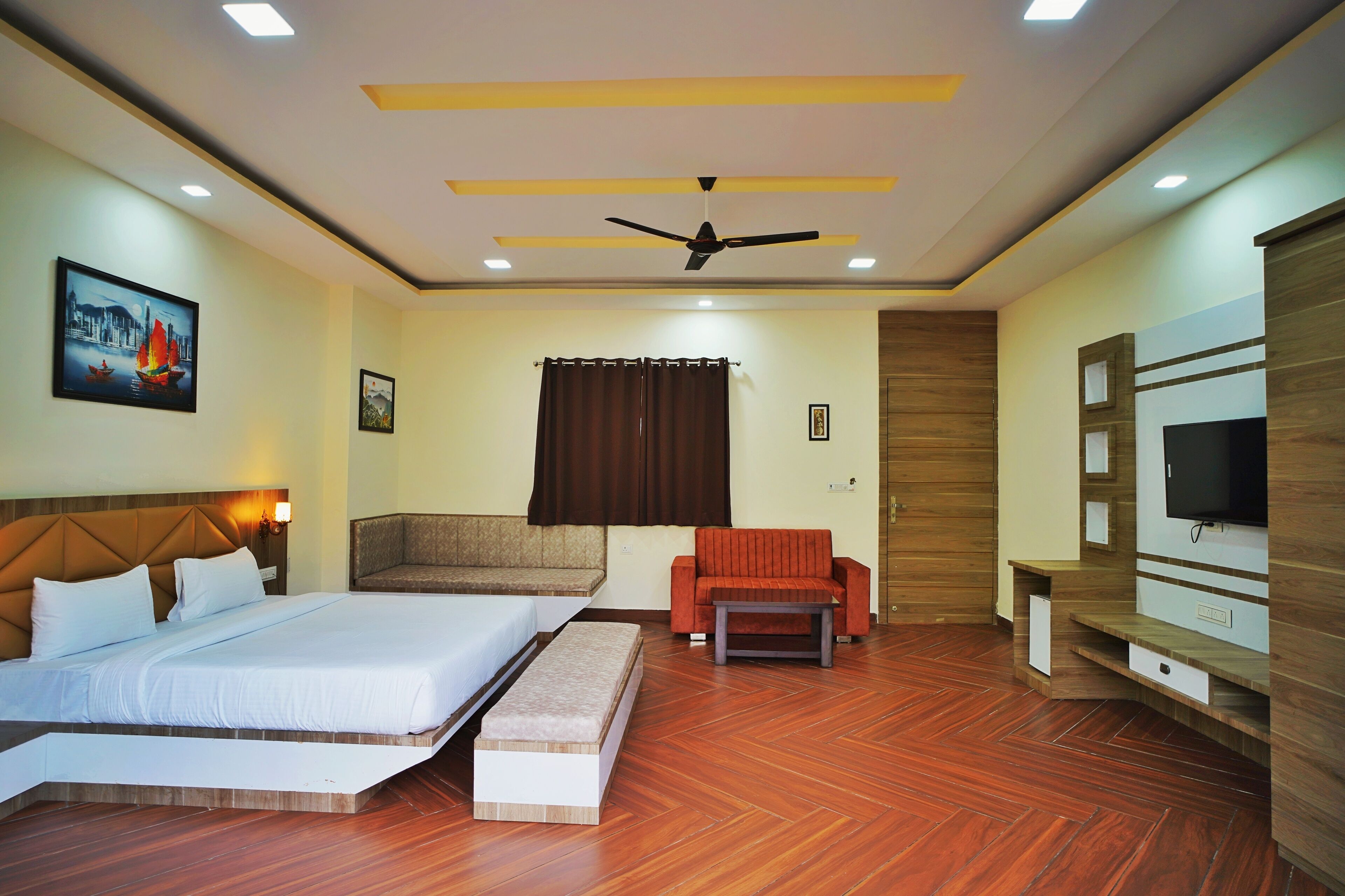 A hotel room with a bed, a sofa, a TV, and a ceiling fan.