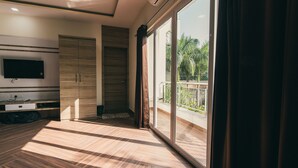 Habitación moderna con un amplio ventanal corredero a un balcón, un televisor de pantalla plana montado en la pared y un armario de madera.