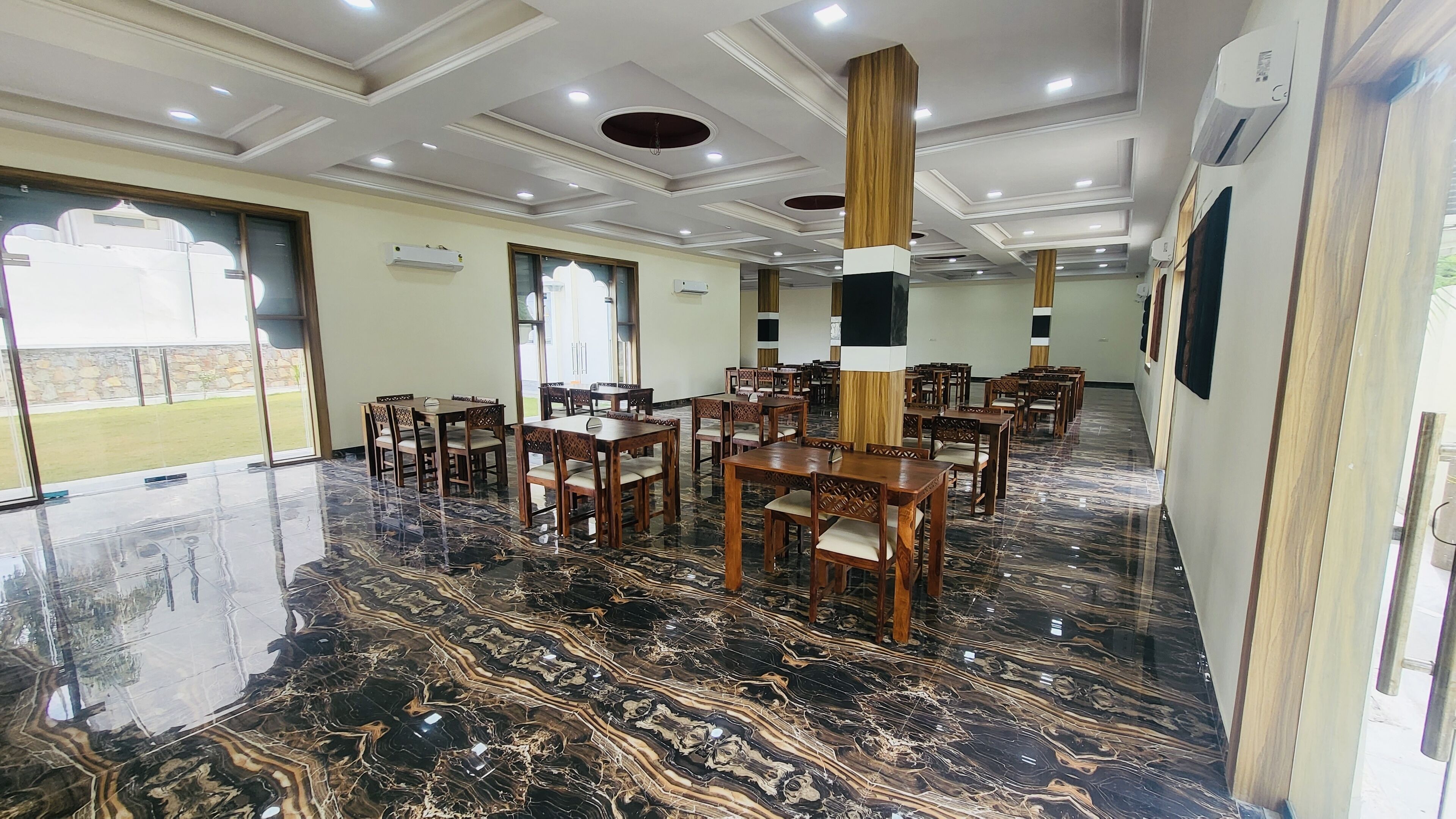 A spacious room with a polished marble floor, wooden tables and chairs, and recessed ceiling lighting.