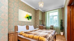 Une chambre à coucher avec un lit en bois, une table de chevet, un bureau avec une chaise, une plante en pot et une fenêtre avec des rideaux.