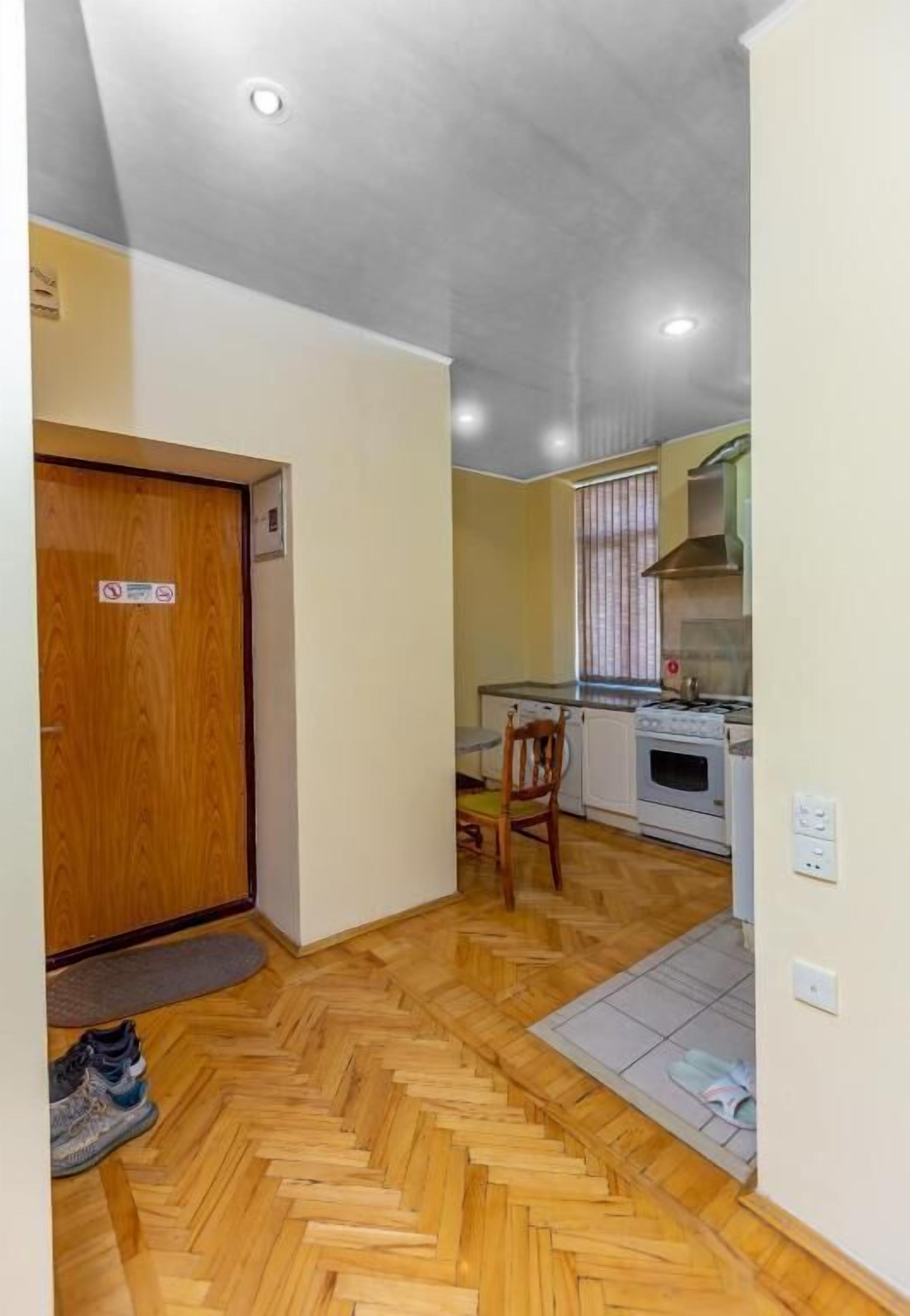 Un pasillo que conduce a una cocina con piso de espiga, una puerta de madera y una silla.
