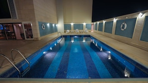 Une piscine intérieure avec un sol carrelé, un escalier d’accès et plusieurs chaises longues disposées le long du bord de la piscine.