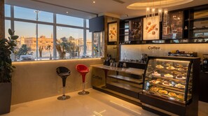 Interior moderno de una cafetería con un ventanal grande, una barra con exhibición de café y dos taburetes.