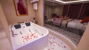 Une salle de bain moderne dotée d’une grande baignoire, d’une douche à parois de verre, et une chambre comprenant un lit et un coin salon.