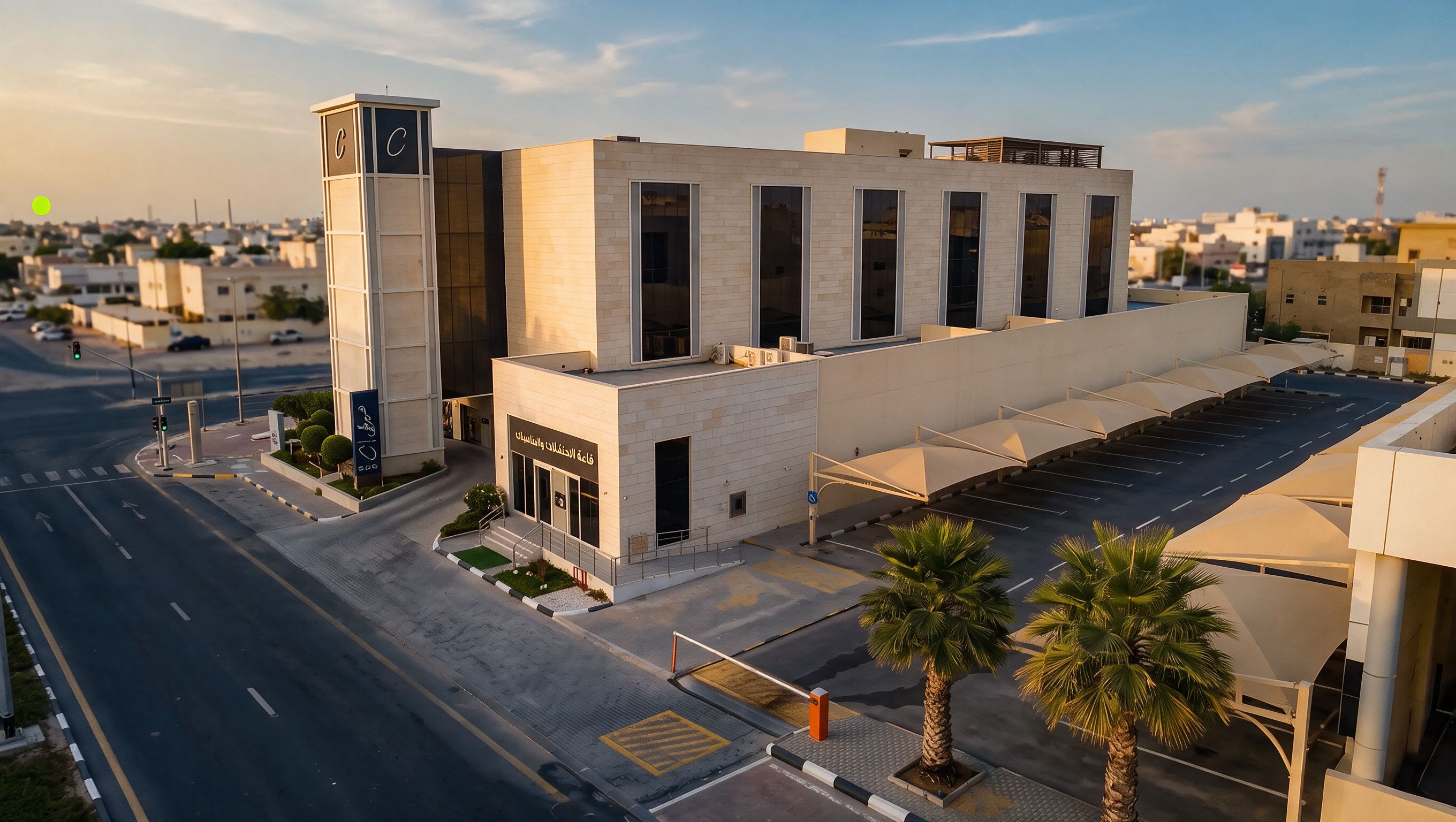 A modern building with a prominent tower, large windows, and a parking area with palm trees.