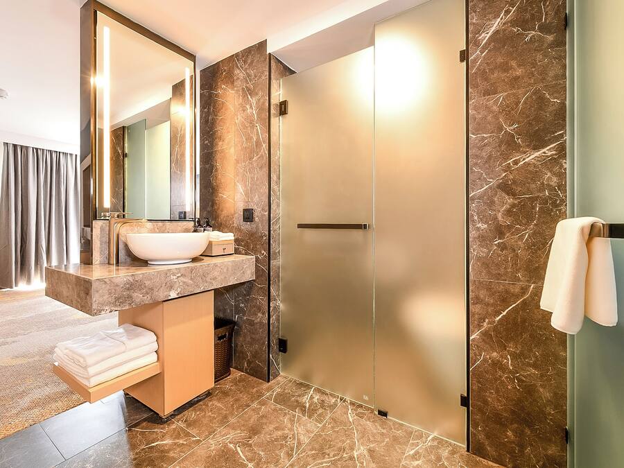 A modern bathroom with a large mirror, a marble sink, and a glass shower enclosure.