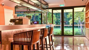 Zona de bar con mostrador de mármol, taburetes de madera y vista a un jardín a través de amplios ventanales.