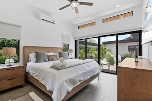 Une chambre moderne avec un grand lit, un ventilateur de plafond et une vue sur l’extérieur.