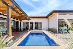 Une maison moderne dotée d’une piscine, d’une terrasse en bois et d’un patio couvert.