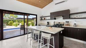 Una cocina moderna con una isla grande, armarios oscuros y vistas a una piscina.