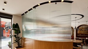 Una moderna recepción con un banco de madera curvado, un separador de vidrio y una planta en maceta.