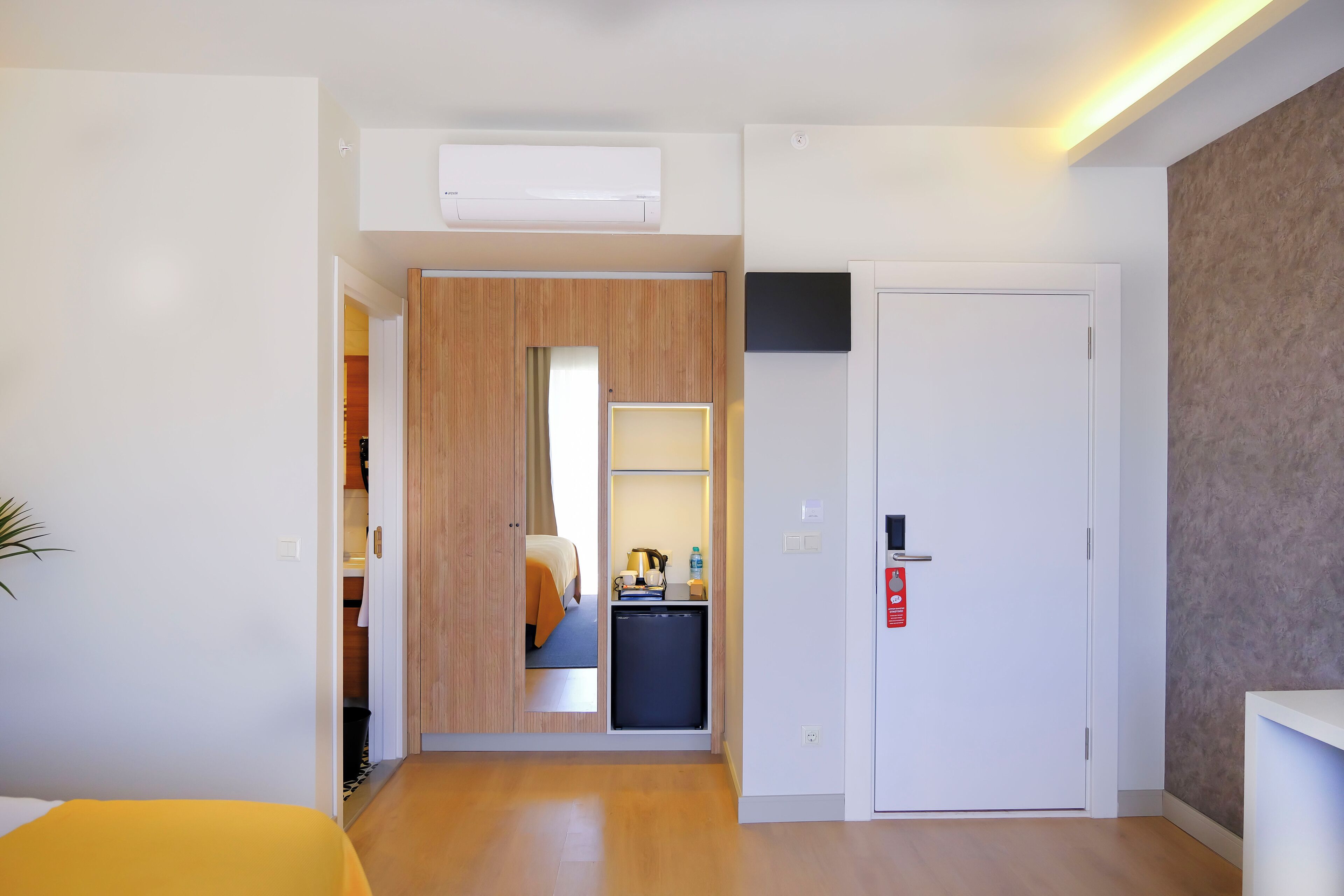 Habitación de hotel compacta con armario de madera, kitchenette pequeña, cama y una puerta blanca.