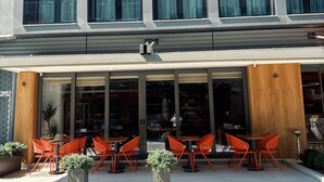 Un edificio moderno con amplios ventanales y una zona de estar exterior cubierta con sillas naranjas.
