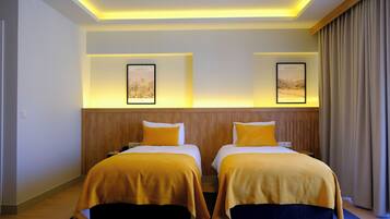 Ein Hotelzimmer mit zwei Betten, jeweils mit gelber Bettdecke, einem Holz-Kopfteil und zwei gerahmten Bildern an der Wand.