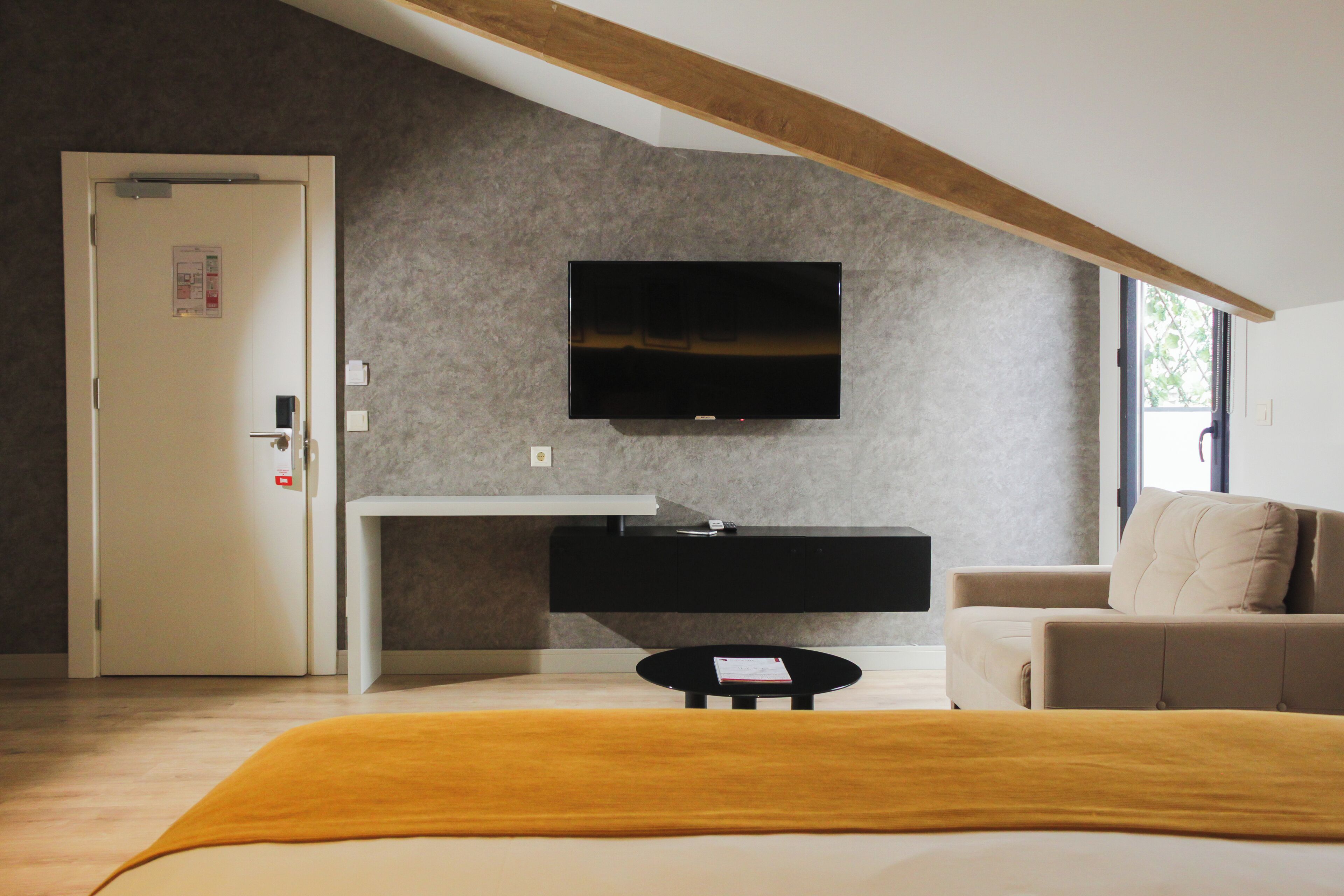 Un dormitorio moderno con una cama, una mesita de noche, un televisor montado en la pared y una puerta.