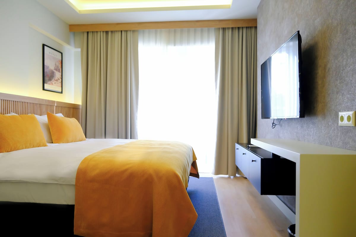 Hotellihuone, jossa on suuri sänky, taulutelevisio, työpöytä tuolilla sekä ikkuna, jossa on verhot.