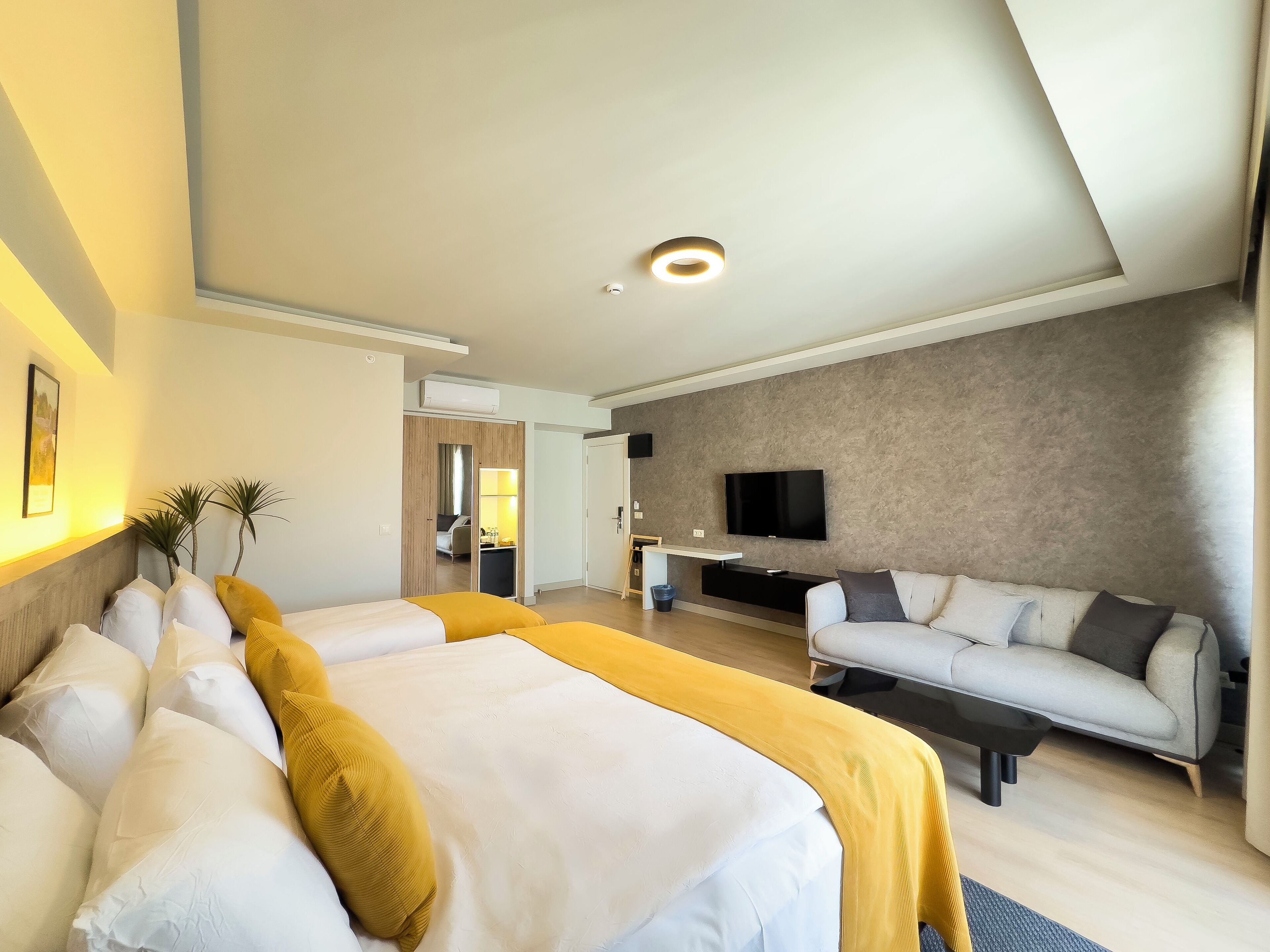 Quarto de hotel moderno com uma cama grande, um sofá, uma TV de tela plana e uma pequena área de trabalho.
