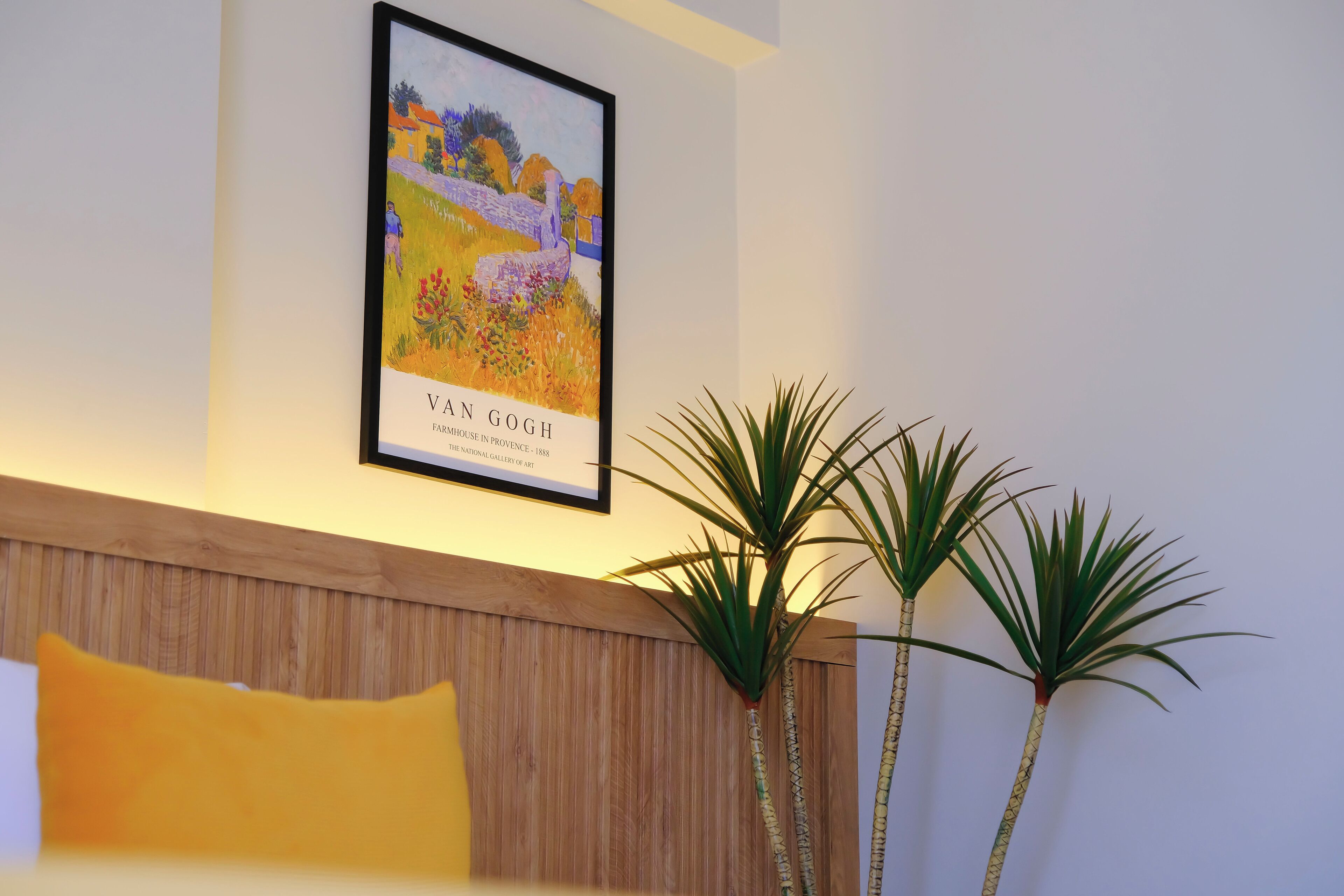 A framed Van Gogh painting, a wooden headboard, and two tall plants in a room.