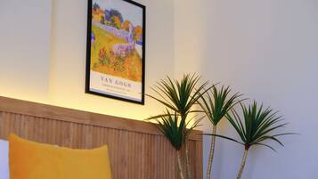 A framed Van Gogh painting, a wooden headboard, and two tall plants in a room.