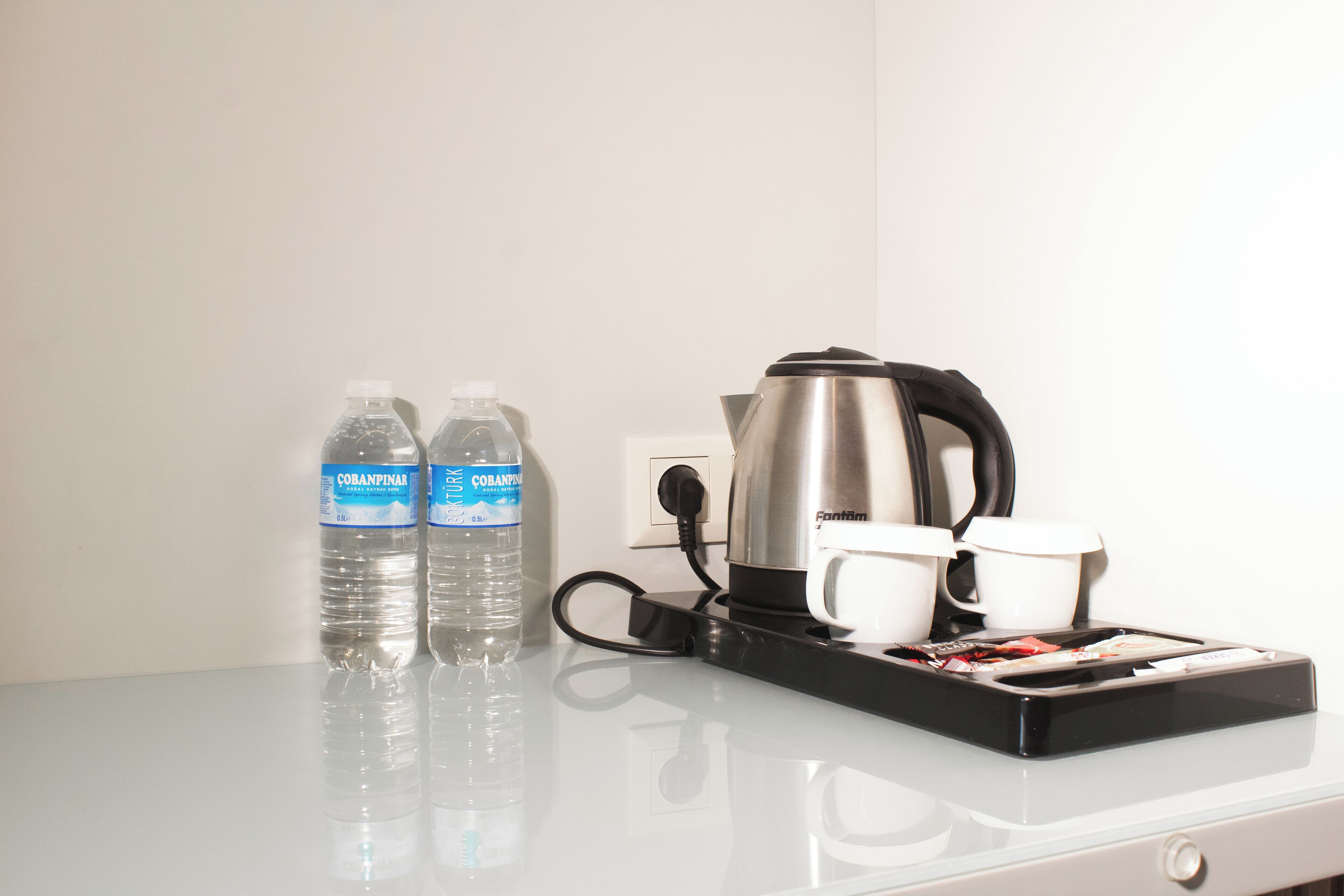 A hotel room with a coffee maker, two water bottles, and two white cups on a table.