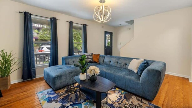 A living room with a blue sectional sofa, a wooden coffee table, and a chandelier. - 10 Mins to Downtown, 4BR + Game Room + 3 Baths (Pittsburgh)