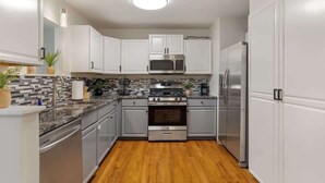 A modern kitchen with white cabinets, stainless steel appliances, a wooden floor, and a tiled backsplash. - 10 Mins to Downtown, 4BR + Game Room + 3 Baths (Pittsburgh)