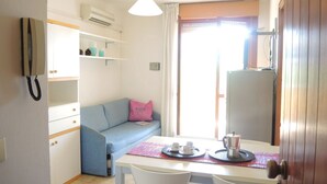 A compact kitchenette with a fridge, a small table with a coffee pot, and a blue sofa with a pink pillow. - Fantastic one Bedroom Apartment With Swimming Pool (San Michele al Tagliamento)