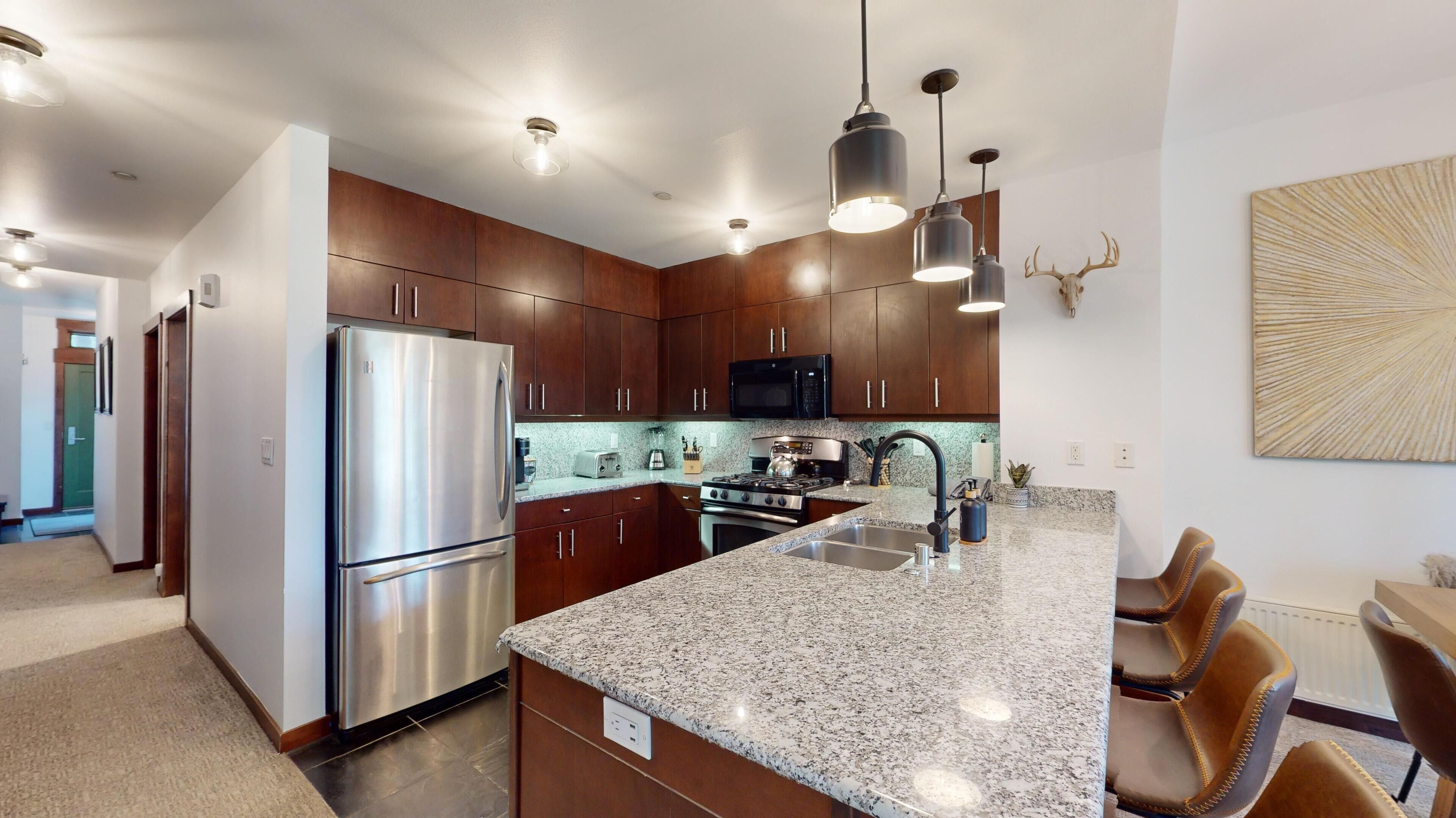 A modern kitchen with stainless steel appliances, granite countertops, and dark wooden cabinets.