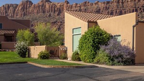 Un edificio residencial con techo plano, un pequeño jardín delantero y vistas a una cadena montañosa.