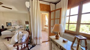 A bedroom with a bed, a wooden chair, a bedside table with a lamp, and a window with curtains. - Magnifica Villa 5 Bed La Font With Private Pool (Sant Joan d'Alacant)