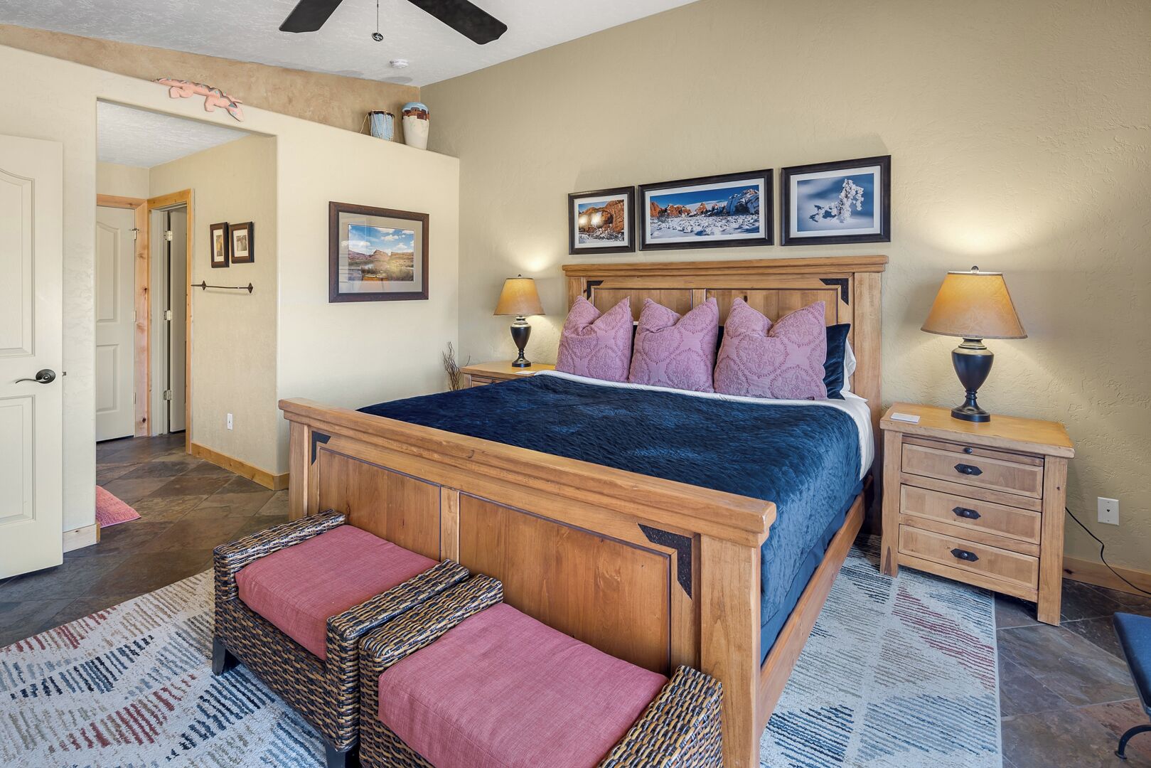 A bedroom with a wooden bed, two bedside tables, a nightstand, a patterned rug, and framed pictures on the wall.