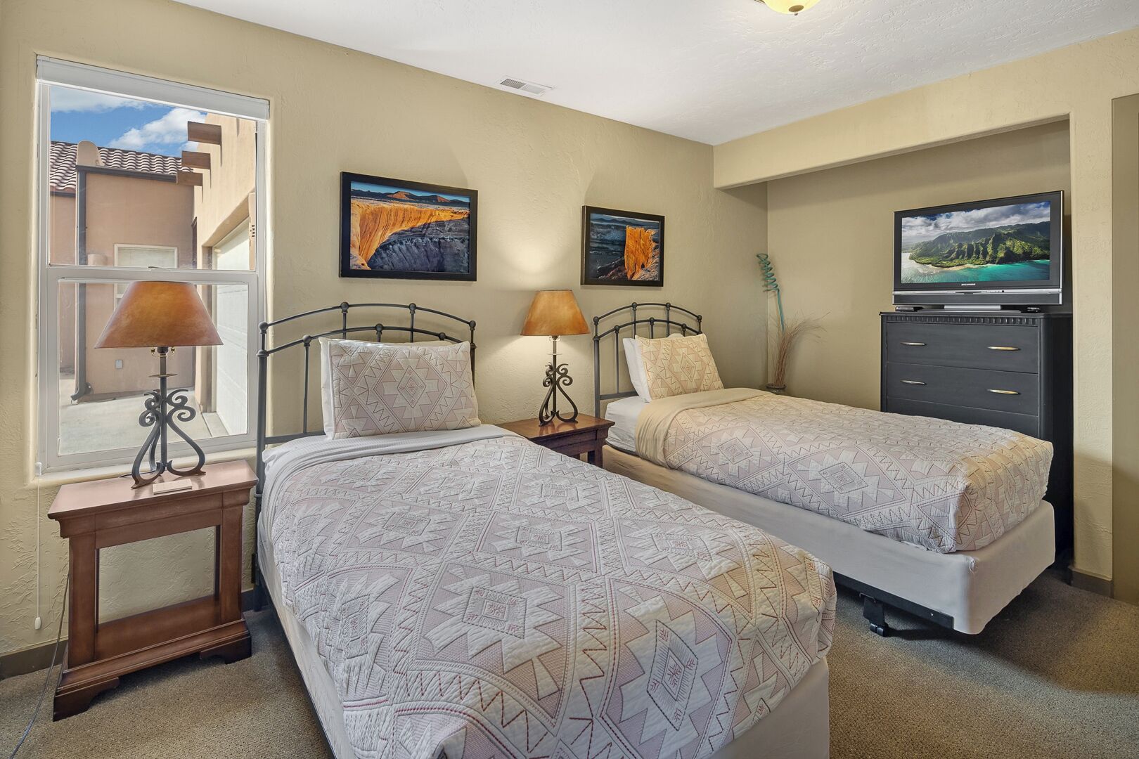 A bedroom with two beds, a TV, and artwork on the walls.