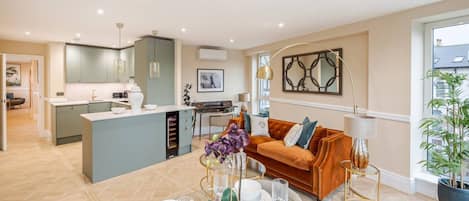 A modern kitchen with a central island, a dining area with a glass table, and a cozy living space with a sofa and a lamp.