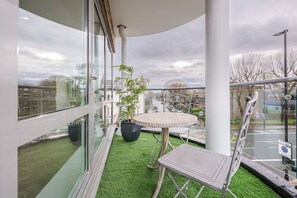 A balcony with a glass railing, a round table, a potted plant, and a chair.