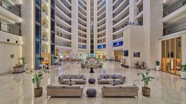 A spacious lobby with multiple floors, a central seating area, and a modern design. - Regenta - The World Surat (Surat)